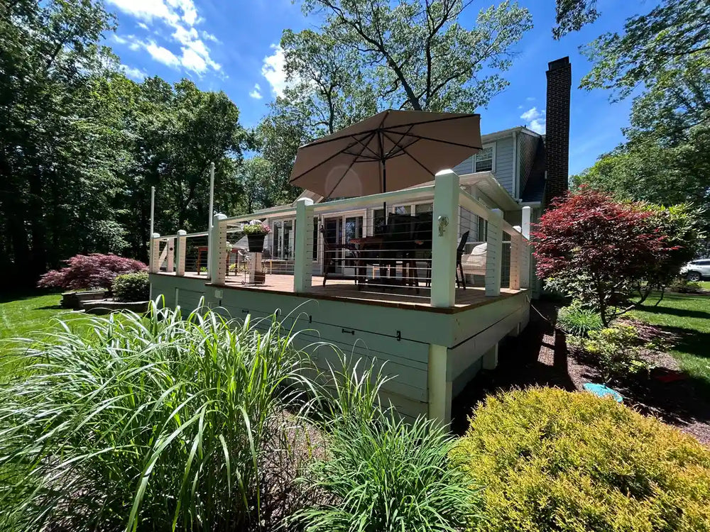 A quiet garden view seen through stainless steel cable railing on a wood deck