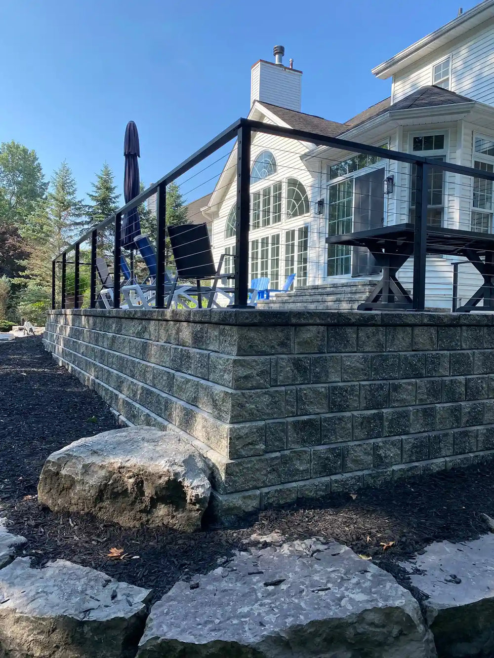 angled view of wire railing installed along a raised stone patio in the backyard