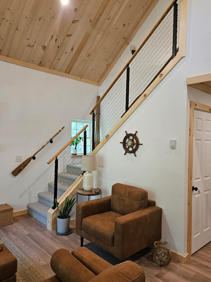 Black stair cable railing with wood handrail and nautical oar decor in cozy lakeside home.