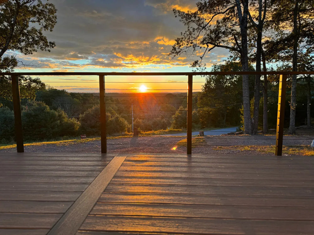 black deck railing overlooking a sunset view across trees and open landscape.