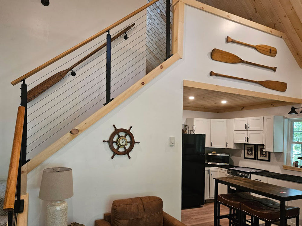 Sleek stair cable railing overlooking kitchen with decorative paddles and ship's wheel clock.