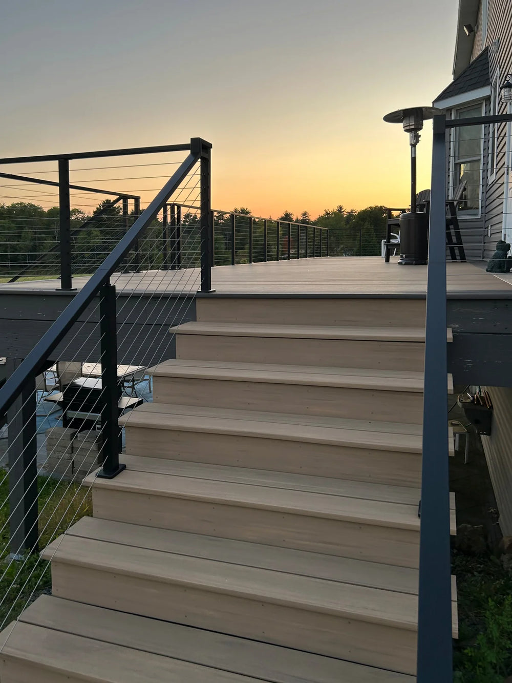 staircase with wire deck railing leading up to a sunset-lit deck