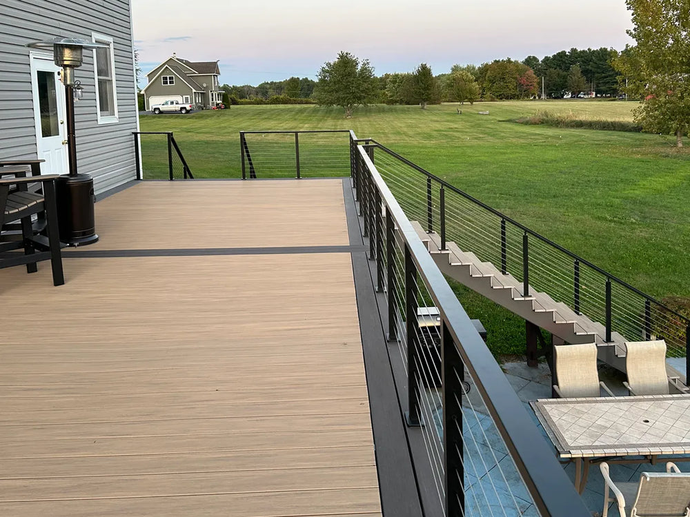 wide backyard deck with modern wire deck railing overlooking an open green field
