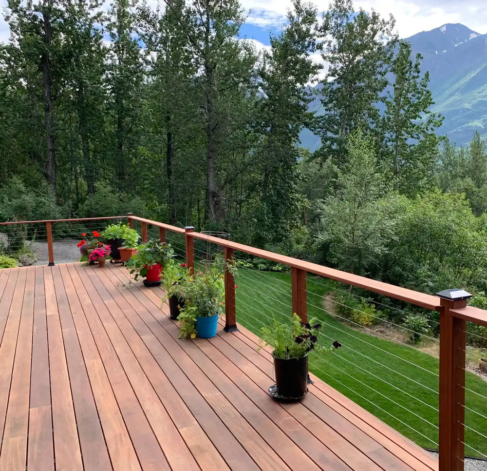 wood deck with cable railing and potted plants facing a green forest